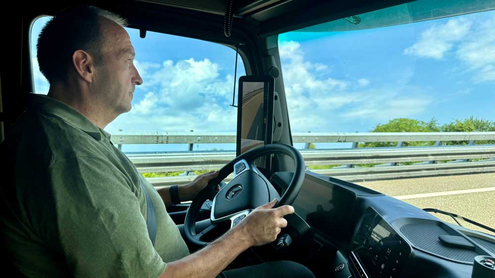 Lächeln auf die Lippen 
Der Fahrer thront luftgefedert  in einer geräumigen Kabine, blickt auf ein halbes Dutzend Kamera-Monitore - und braucht nicht viel mehr als den kleinen Finger und den großen Zeh, um den Sattelzug in Fahrt und auf Kurs zu halten. 